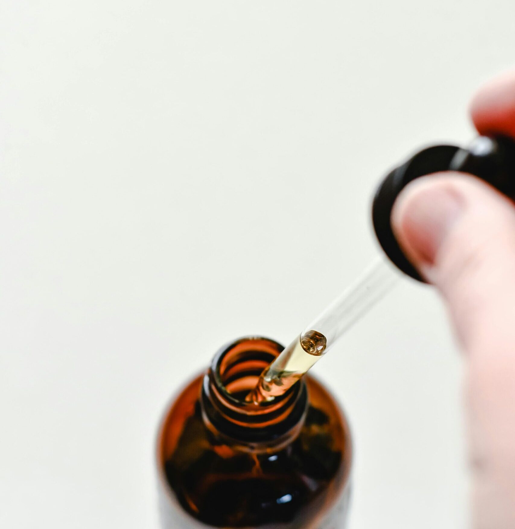 About Premium Green Extracts Close-up of a glass dropper with liquid above an amber bottle on a light background.